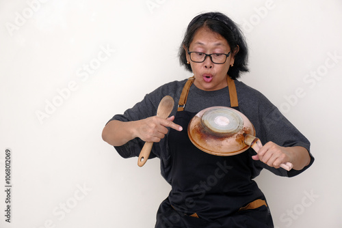 Asian housewife holding a frying pan and wooden spatula, showing how bad the pan is burnt photo