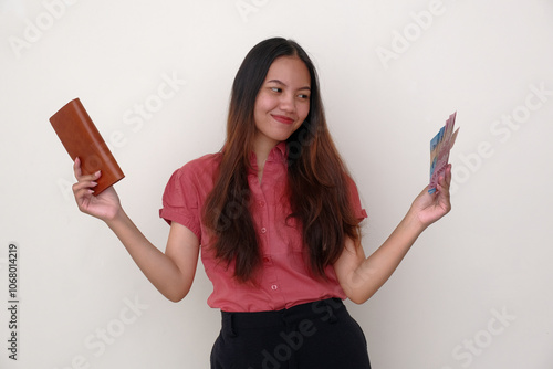 Female young Asian girl standing alone happily showing a leather wallet and some cash Rupiah money in her hands photo