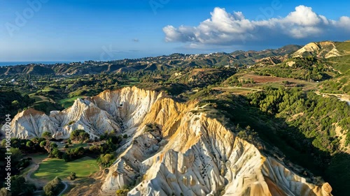 An aerial view of the rugged, white and yellow cliffs of the Avakas Gorge in Cyprus, with a green golf course in the foreground photo