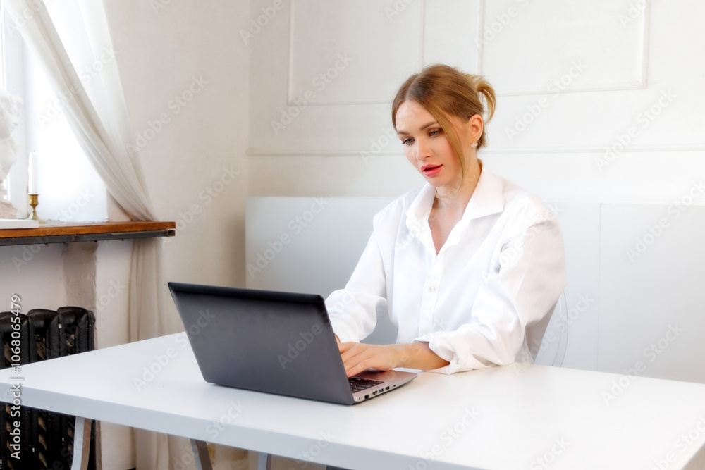 A woman working on a laptop at a bright desk in a minimalist room during the day A woman working on a laptop at a bright desk in a minimalist room during the day