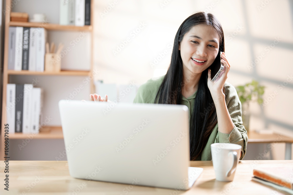 Woman working on laptop at home office while talking on phone, warm light Woman working on laptop at home office while talking on phone, warm light