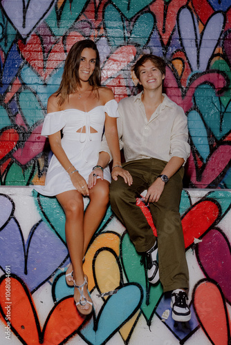 A couple kisses in front of a vibrant heart mural, symbolizing their love in a lively urban setting