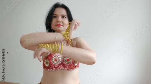 A dancer in a red suit is dancing an oriental dance on a white background. A professional dancer dances oriental belly dance. Sexy woman in red dress dances a seductive dance in a white studio