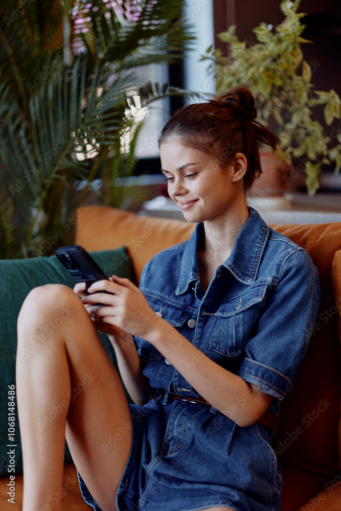 Young woman sitting on a comfortable sofa with legs crossed and using a smartphone at home Young woman sitting on a comfortable sofa with legs crossed and using a smartphone at home