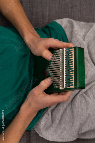 Man playing green kalimba at home, seeking calm through meditative melodies. Close-up on kalimba keys as soothing sounds fill the room, finding peace in every note
