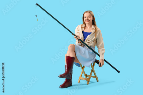 Happy young woman with fishing rod sitting on stool against blue background photo