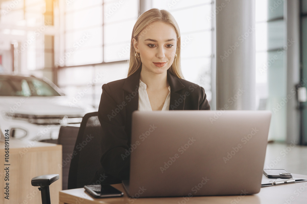 Smiling saleswoman typing on her laptop at new car showroom Smiling saleswoman typing on her laptop at new car showroom