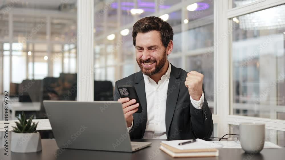 Businessman celebrates success while using phone and laptop in office. Man expresses joy and excitement about achievement. Mobile win, excited overjoyed lucky executive winner receive good news. Businessman celebrates success while using phone and laptop in office. Man expresses joy and excitement about achievement. Mobile win, excited overjoyed lucky executive winner receive good news.
