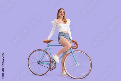 Beautiful young happy woman with bicycle on purple background