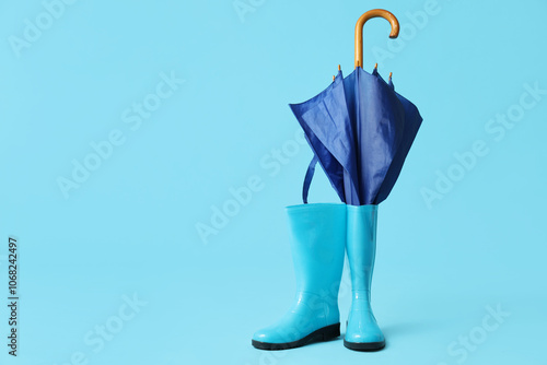 Stylish umbrella and gumboots on blue background