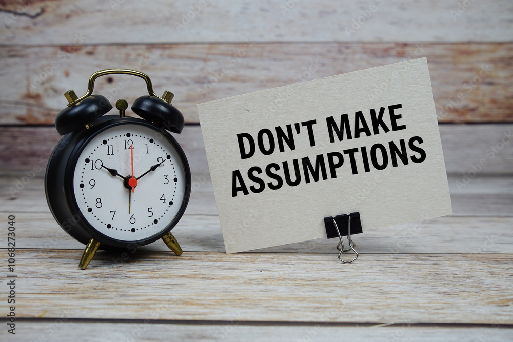 Don't make assumptions text on paper card with alarm clock on wooden background Don't make assumptions text on paper card with alarm clock on wooden background