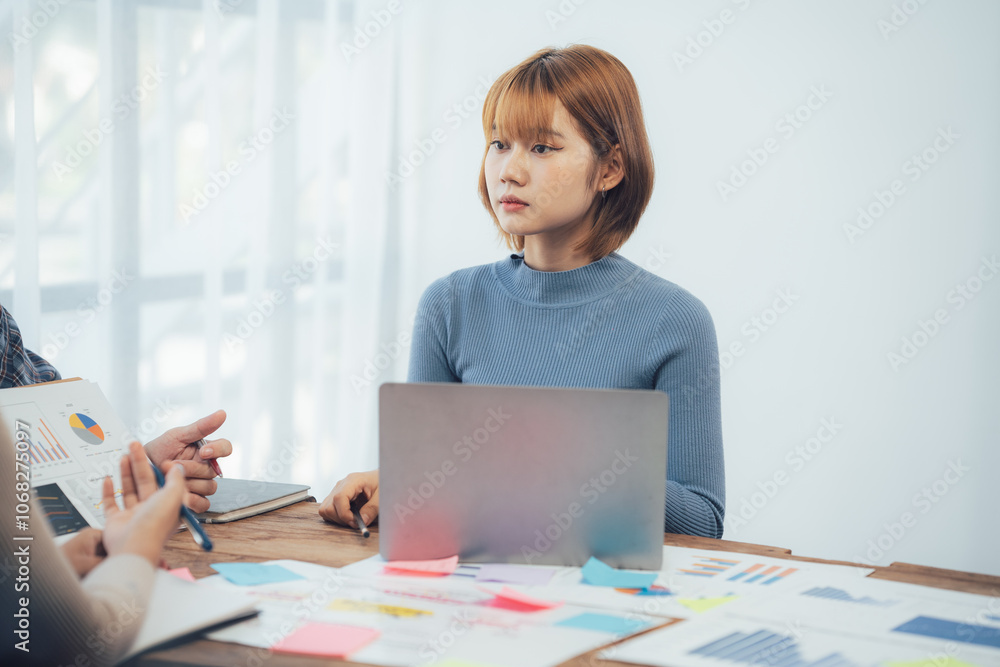 Focused on the Task: A young Asian businesswoman attentively listens during a business meeting, her concentration evident as she takes in information and considers her next move. Focused on the Task: A young Asian businesswoman attentively listens during a business meeting, her concentration evident as she takes in information and considers her next move.