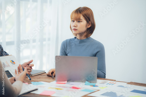 Focused on the Task: A young Asian businesswoman attentively listens during a business meeting, her concentration evident as she takes in information and considers her next move. 