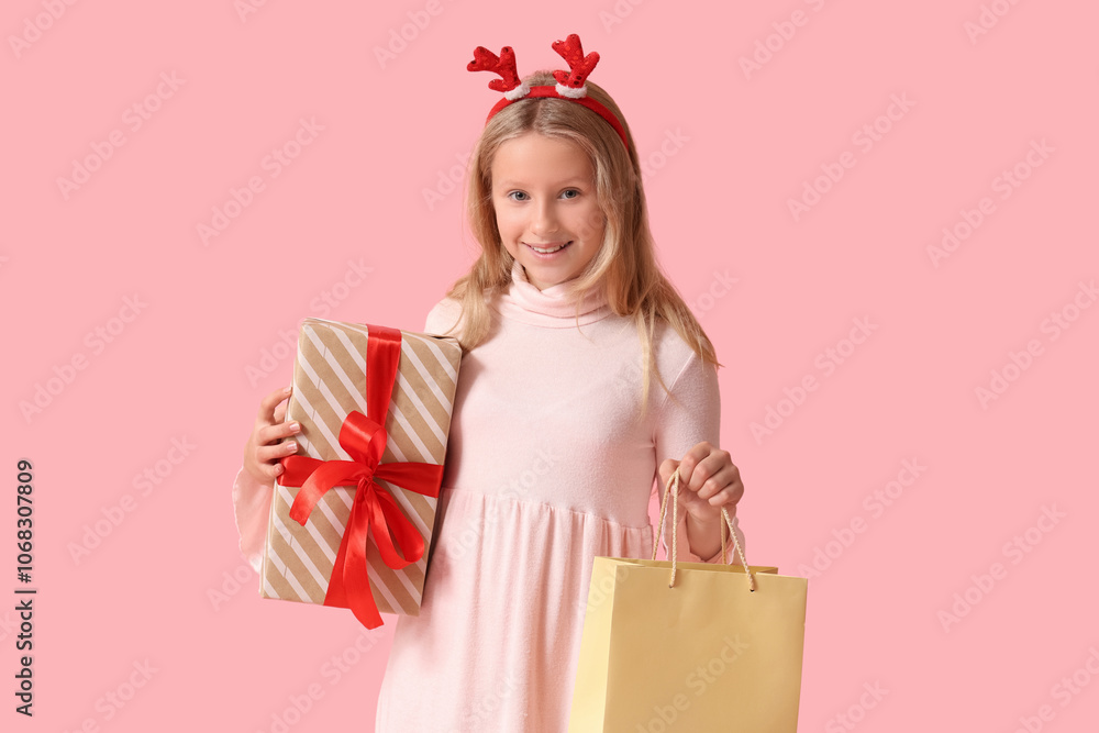 Cute girl in reindeer horns with shopping bag and gift box on pink background. Christmas celebration Cute girl in reindeer horns with shopping bag and gift box on pink background. Christmas celebration