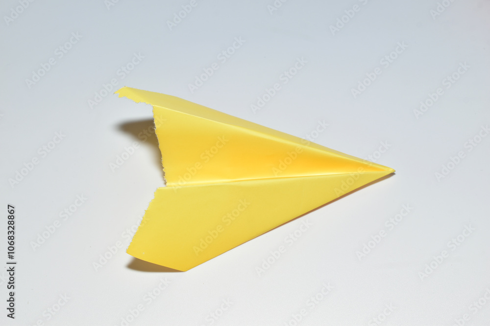 A yellow paper airplane lies on a white background. A yellow paper airplane lies on a white background.