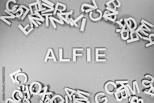 Alfie popular and modern baby boy fashion name in wooden English language capital letters scattered from a pile of letters on a green background in black and white photo