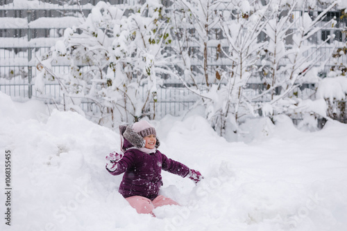 Little girl wearing a cozy winter outfit, happily exploring deep snow. The pure white snow surrounds her, creating a dreamy winter scene full of childhood wonder