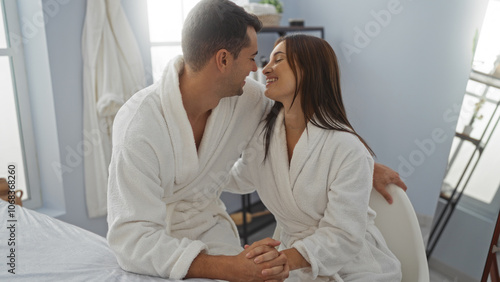 Couple relaxing in spa wearing robes, smiling at each other in a cozy indoor wellness room indicating love and intimacy