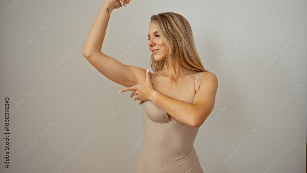 Fototapeta premium Woman making arm flex gesture showcasing strength against an isolated white background, emphasizing beauty and confidence in a blonde, young, adult, attractive, female.