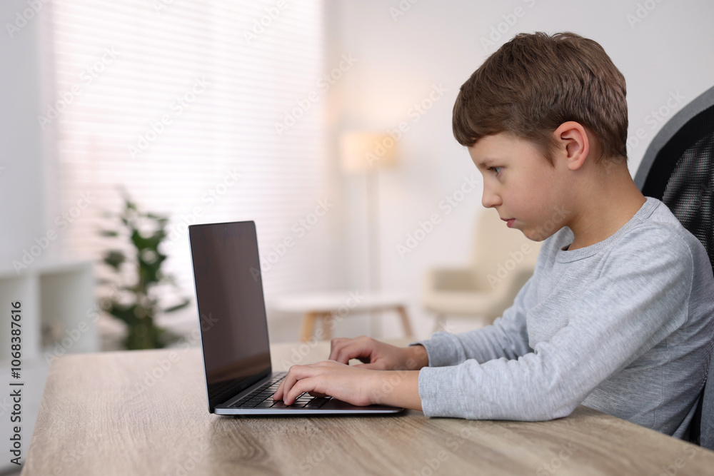 Boy with incorrect posture using laptop at wooden desk indoors Boy with incorrect posture using laptop at wooden desk indoors
