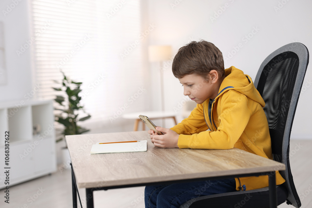 Boy with incorrect posture using laptop at wooden desk indoors Boy with incorrect posture using laptop at wooden desk indoors