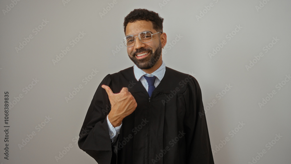 Young man in graduation gown smiling and pointing thumb over isolated white wall background Young man in graduation gown smiling and pointing thumb over isolated white wall background