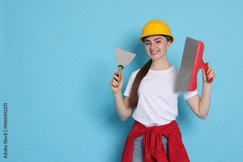 Portrait of young decorator with putty knives on light blue background, space for text Portrait of young decorator with putty knives on light blue background, space for text