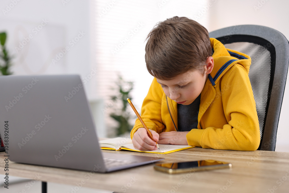 Boy with incorrect posture using laptop at wooden desk indoors Boy with incorrect posture using laptop at wooden desk indoors