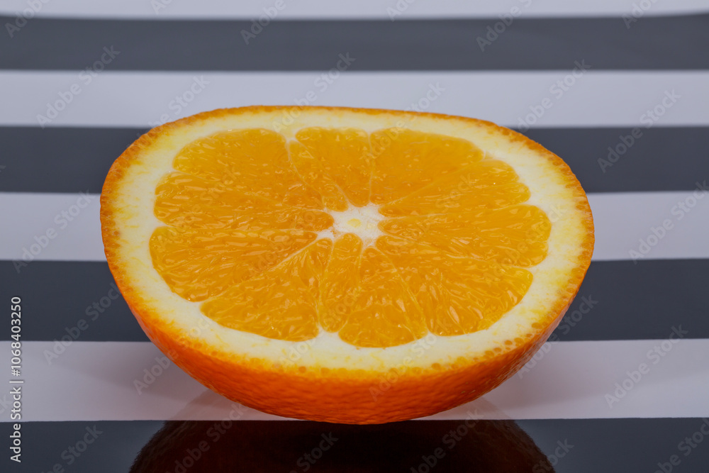 Half a fresh orange lying on a black and white striped tablecloth, close up