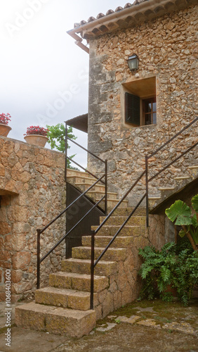 Stone staircase leading up to the entrance of a rustic stone house with flower pots and greenery, showcasing mediterranean architecture