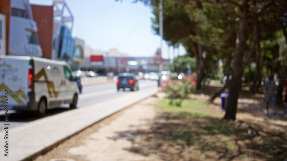 Obraz premium Blurred outdoor urban scene with defocused cars, people, trees, and buildings under a bright sunny sky
