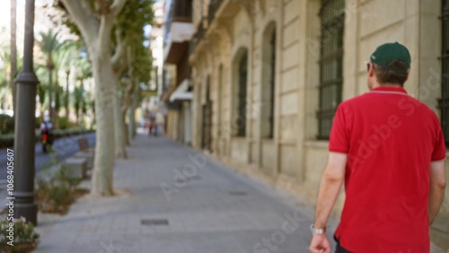 Man walking along a tree-lined urban street with blurred background and historic buildings in an out-of-focus scene capturing a defocused pedestrian on a sunny day.