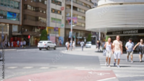 Blurred urban street with defocused pedestrians including men and women walking on a sunny day with buildings and cars in the background