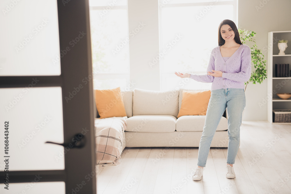 Full size photo of attractive young teen woman hands point welcome dressed purple outfit bright cozy day light home interior living room Full size photo of attractive young teen woman hands point welcome dressed purple outfit bright cozy day light home interior living room