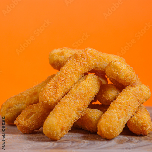 Pile of crispy breaded cheese sticks on a wooden surface against an orange background. Studio food photography. Snack and appetizer concept. Design for poster, banner, menu, wallpaper.