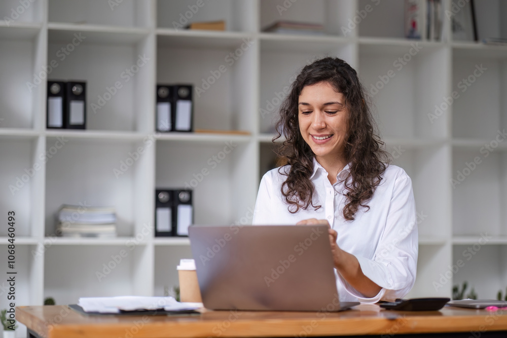 Confident Businesswoman Working on Laptop in Modern Office Environment with Shelves and Documents in Background Confident Businesswoman Working on Laptop in Modern Office Environment with Shelves and Documents in Background