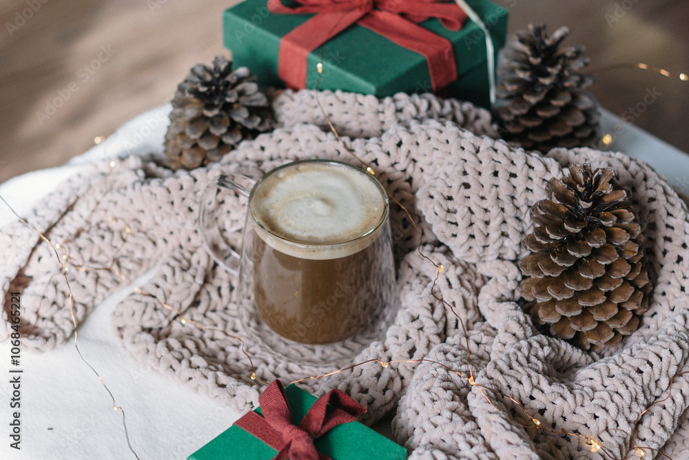 Winter still life. A glass cup of coffee with milk, big cones, lights, a green gift box with a red bow. Modern christmas rustic eco friendly decor, scandinavian winter hygge. Atmospheric christmas