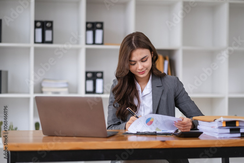 Confident Businesswoman Analyzing Reports at Modern Office Desk with Laptop and Documents