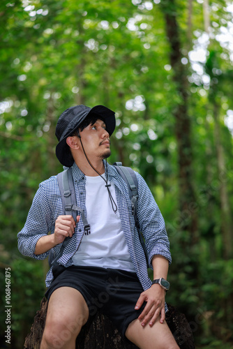 portrait of asian man sitting on a tree in rain forest looking up sky.