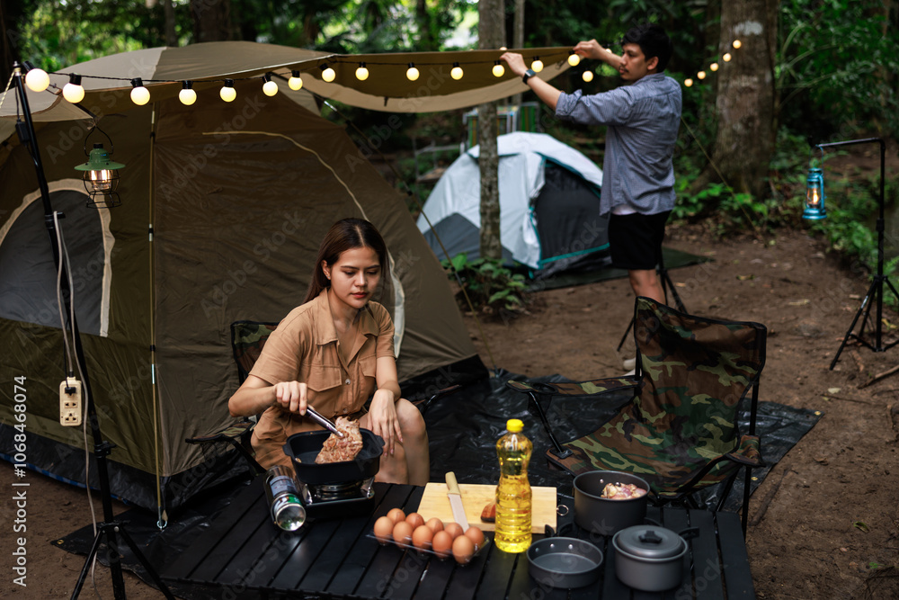 asian woman grilling meat on a portable gas stove while camping in nature park at evening time. Travel, adventure and vacation concept asian woman grilling meat on a portable gas stove while camping in nature park at evening time. Travel, adventure and vacation concept
