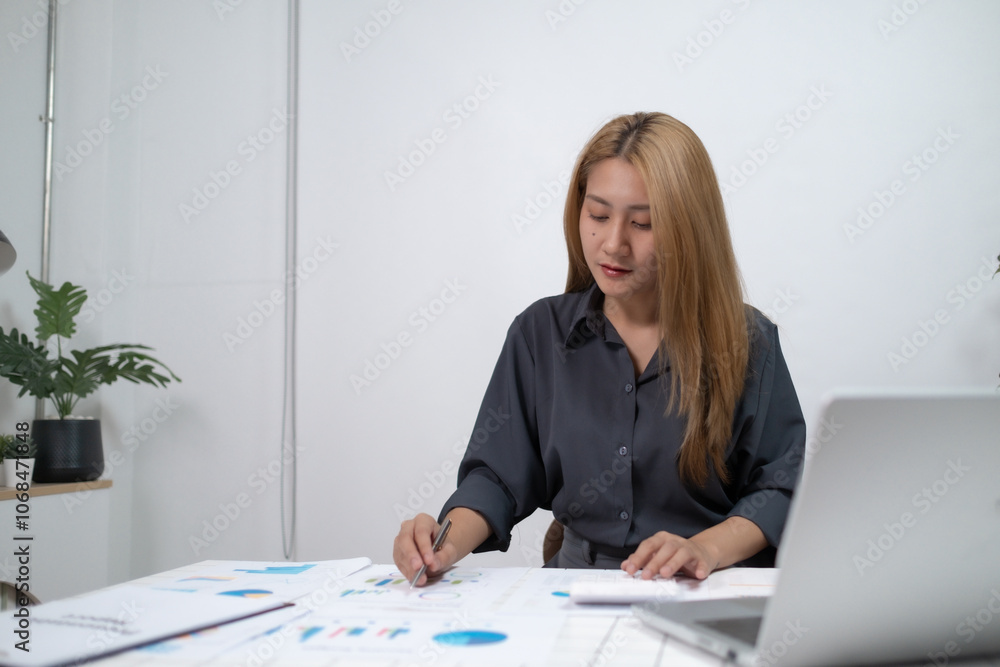 A woman is sitting at a desk with a laptop and a stack of papers A woman is sitting at a desk with a laptop and a stack of papers