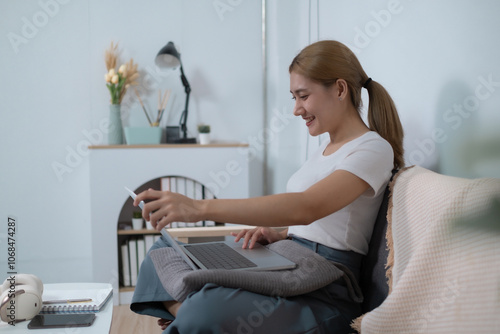 A woman is sitting on a couch with a laptop and a cell phone in her hands