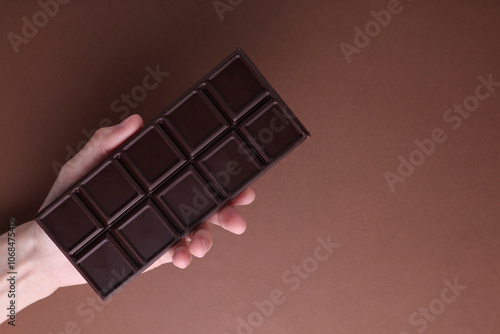 HAnd holding Dark chocolate bar on brown background photo