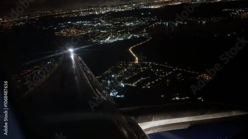 View from cabin of airplane with marker lights flying over night cityscape with river and bridge. Flying passenger plane over modern city in darkness. Business flights between cities. Grain texture