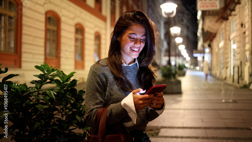 Fotografie Happy woman walking through the brightly lit city streets and using phone