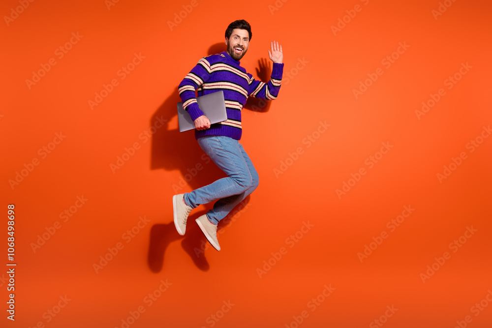 Naklejka premium Full size photo of nice young male jump hold netbook wave hand wear trendy striped violet outfit isolated on orange color background