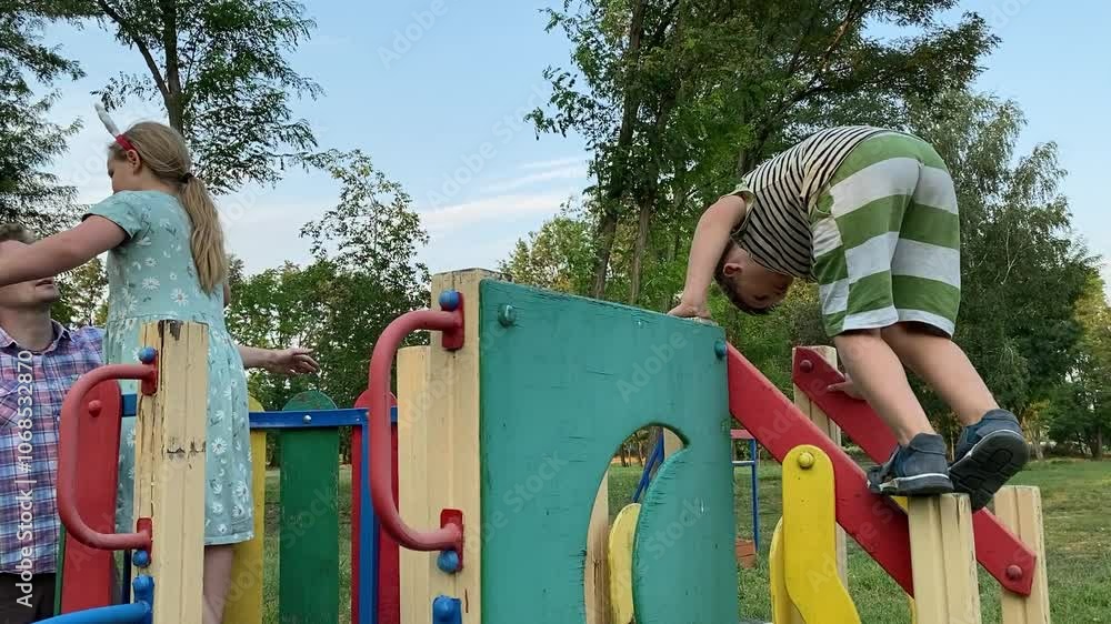 A young father enjoys quality time with two elementary aged children at outdoor playground on a warm summer day. The family engages in fun activities, laughter, play, the most of leisure time together A young father enjoys quality time with two elementary aged children at outdoor playground on a warm summer day. The family engages in fun activities, laughter, play, the most of leisure time together