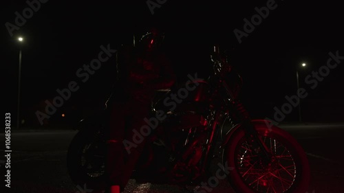 Biker poses near his motorcycle with his arms crossed over chest. Reflections of night lights in tinted visor of helmet. Motorcycle as part of lifestyle. Subculture of motorcycle lovers and admirers photo