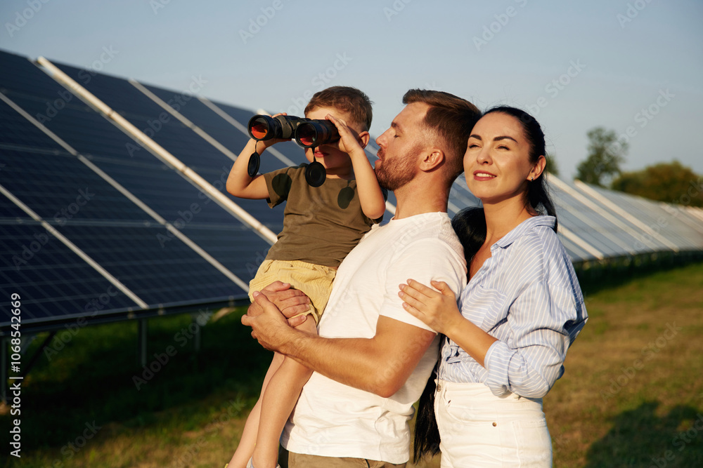 Looking through the binoculars. Father, mother and little son are outdoors near solar panels Looking through the binoculars. Father, mother and little son are outdoors near solar panels