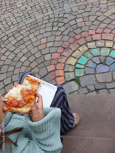 Child sitting on steps eating pizza, in front of a rainbow